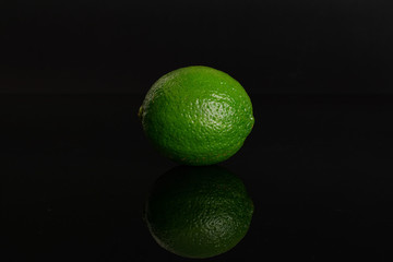 One whole fresh green lime isolated on black glass