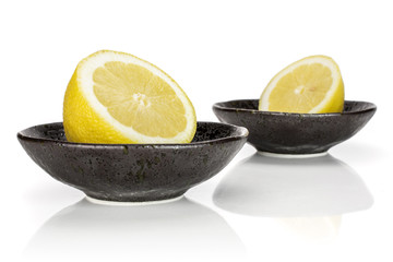 Group of two halves of fresh yellow lemon one is in the front and both are in a dark ceramic bowl isolated on white background