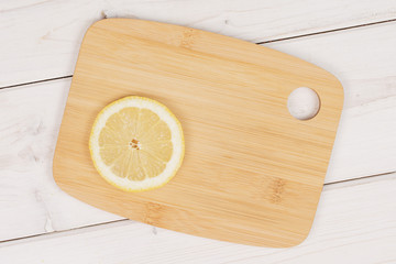 One slice of fresh yellow lemon on a bamboo cutting board flatlay on white wood