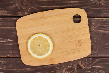 One slice of fresh yellow lemon on a bamboo cutting board flatlay on brown wood