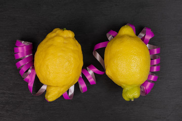 Group of two whole fresh yellow lemon with a pink ribbon flatlay on grey stone