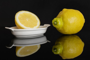 Group of one whole one half of fresh yellow lemon in a white oval ceramic bowl isolated on black...