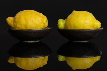 Group of two whole fresh yellow lemon in a dark ceramic bowl isolated on black glass