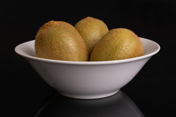 Group of three whole fresh green kiwifruit actinidia deliciosa in a white ceramic bowl isolated on black glass
