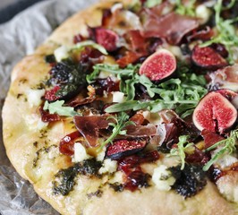 pizza with figs and prosciutto. different cheeses and gorgonzola, basil dressing with olive oil, onion marmalade (caramelized onion), arugula, balsamic sauce. close-up.