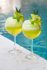  Two glasses of pineapple cocktail next to the pool