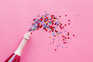 Party with champagne bottle and colorful party streamers on pink background top view