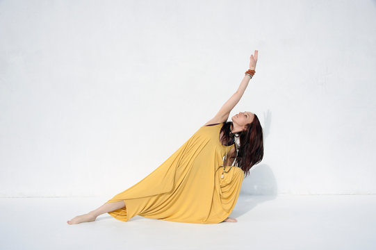 Spiritual woman in yellow outfit dancing photographed on a white background. 