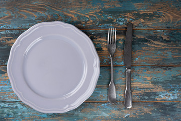 Empty plate with fork and knife on colored wooden background, top view, copy space, mock-up