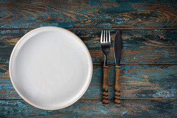 Empty plate with fork and knife on colored wooden background, top view, copy space, mock-up