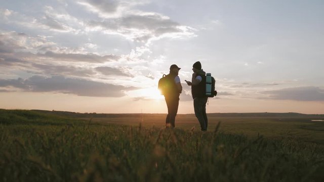 The Silhouette of two man on the top of mountain with Backpacks and other Gear expressing Energy and Happiness. Two tourist young men on rocky cliff and enjoying view. Travel concept.