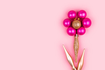 Pink balls and gold Christmas decorations shaped flower on pink background.  Holiday and celebration concept for postcard or invitation.