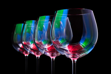 Nightclub wine glasses lit by red, green, blue party lights, nightlife and entertainment industry, four object in row isolated on black background