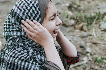 a refugee child in the war, a Muslim girl with a dirty face on the ruins, the concept of peace and war, the child is crying and waiting for help.