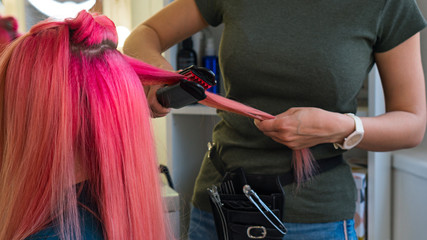 Hairdresser makes hairstyle to client using crimping irons. Hairdressing services. Girl with...