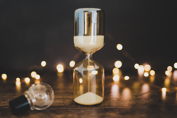 time for new ideas hourglass and lightbulb surrounded by fairy lights bokeh