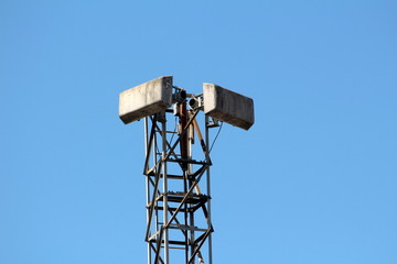 Tall partially rusted strong metal tower with two old antennas mounted on top on clear blue sky background