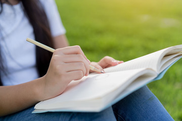 Close up of a female hand writing something on the paper green grass background.women sitting relaxed use pencil and notebook on a green grass in college.