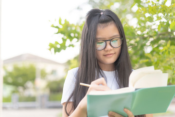 asian female hand writing something on the paper and nature background.teenage smile and relaxed use pencil and notebook in a park nature background