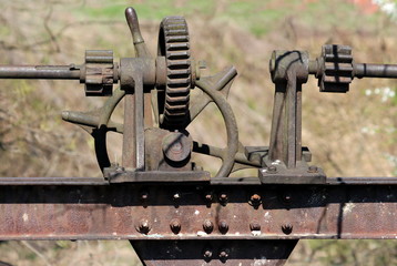 Vintage rusted abandoned dam cogwheel gears and metal poles mounted on heavy beam and connected with multiple screws on warm sunny winter day