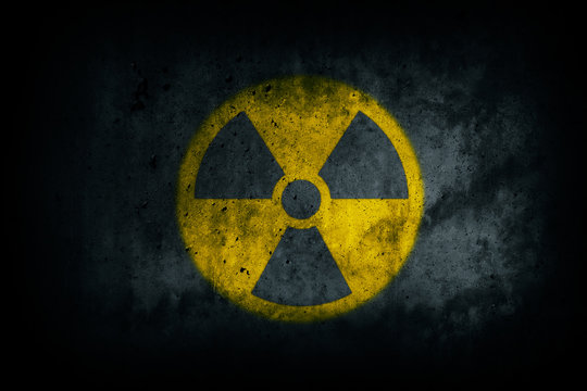Radioactive (atomic nuclear ionizing radiation) danger warning yellow symbol shape painted on massive concrete cement wall grungy texture dark background. Nuclear radioactive alert concept.