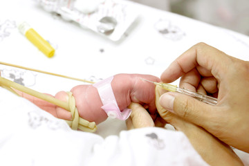 Image of nurse hands uses gradually stabbing IV Catheter (small medical needle for insert injection plug) at sick baby's hands to prepare fill the saline solution and medicine.