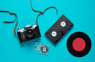 Retro top view still life. Vinyl record, vintage film camera, video and audio cassette on blue background. Flat lay