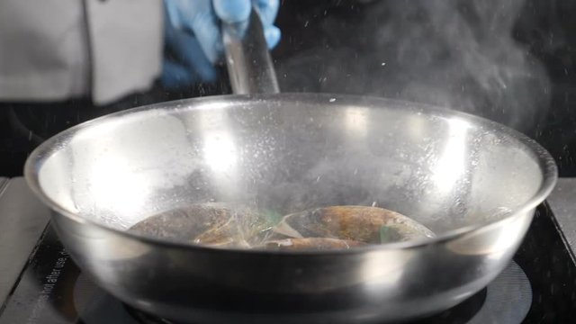 Splendid slow motion food video. chef cooking or tosses seafood in frying pan. Splashes of oil. hd