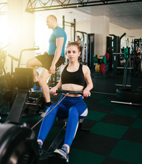 Fototapeta na wymiar Functional training concept. Sport man and woman doing exercise in simulator rowing machine and air bike at gym
