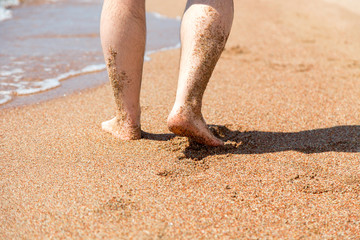 Closeup of bare feet on the beach. Walking on the sand at the water's edge.