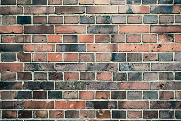 Detail of old and weathered grungy red and gray brick wall marked by the long exposure to the elements as surface texture background.