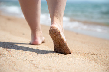 Closeup of bare feet on the beach. Walking on the sand at the water's edge. Vacation and travel concept.