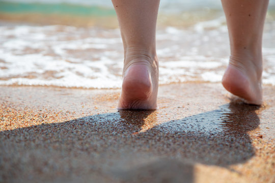 Closeup of bare feet on the beach. Walking on the sand at the water's edge. Vacation and travel concept.
