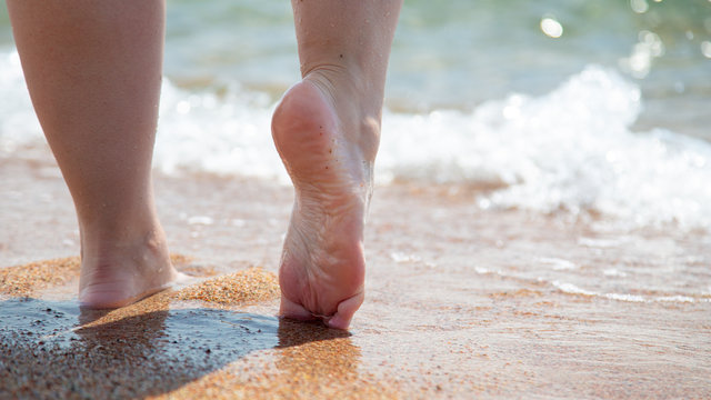 Closeup of bare feet on the beach. Walking on the sand at the water's edge. Vacation and travel concept.