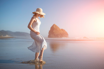 A girl in a hat at sunset near the ocean splashes