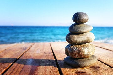 Stones pyramid on over beach wooden deck symbolizing harmony, zen and balance - obrazy, fototapety, plakaty