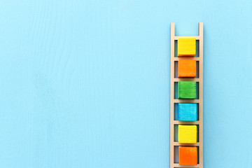 Business image of wooden ladder with colorful cubes over blue table, human resources and management...