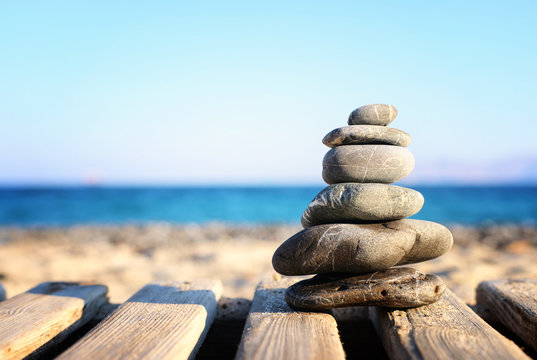 Stones pyramid on over beach wooden deck symbolizing harmony, zen and balance