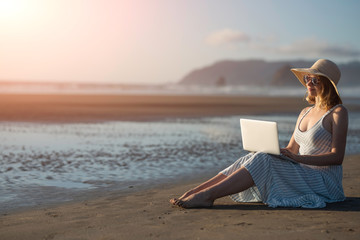 Young girl in sunglasses works on a laptop on the ocean at sunset, freelancing, making money on the...