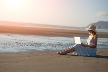 Young girl in sunglasses works on a laptop on the ocean at sunset, freelancing, making money on the Internet, getting money online, lifestyle, Banne, with space