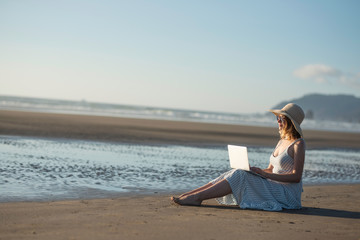 Fototapeta na wymiar Young girl in sunglasses works on a laptop on the ocean at sunset, freelancing, making money on the Internet, getting money online, lifestyle, Banne, with space