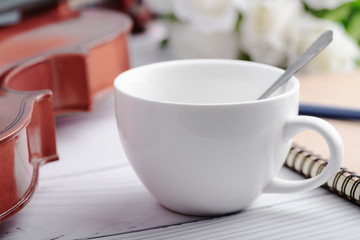 Close-up shot coffee cup and violin orchestra instrumental over white wooden background select focus shallow depth of field