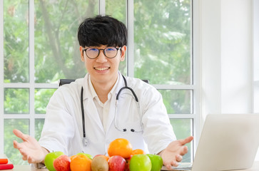 Portrait of smiling asian male nutritionist with healthy fresh organic fruits in his office, healthcare and diet concept