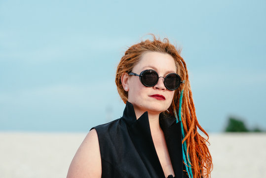 crazy funny grunge punk redhead woman with dreadlocks in office clothes and sunglasses in the desert 