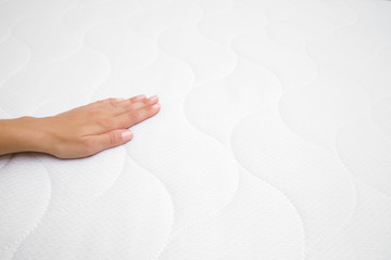 Woman's hand touching cloth of white mattress. Checking softness. Choice of the best type and...