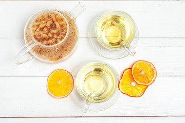 Glass kettle and cup of herbal tea on white wooden background