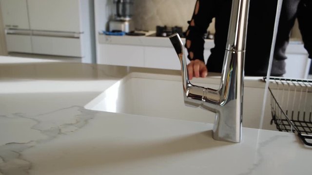 Hand-held pan of caucasian woman turning on water in modern kitchen tap