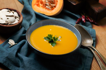 Pumpkin soup in blue bowl with pasrley and seeds.