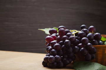 Dark grape in basket on wooden table.