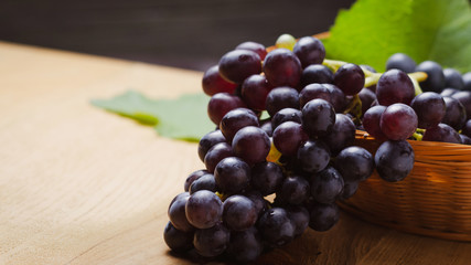 Dark grape in basket on wooden table.